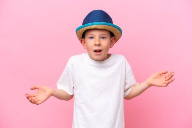 Küçük beyaz çocuk pembe arka planda izole edilmiş bir şapka takıyor ve şok olmuş yüz ifadesi var.