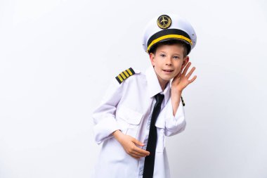 Küçük pilot çocuk beyaz arka planda izole edilmiş bir şekilde kulağına elini sürerek bir şeyler dinliyor.
