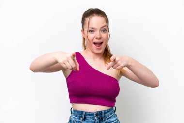 Beyaz arka planda izole genç beyaz kız şaşırmış ve ön tarafı işaret ediyor.