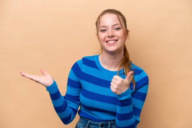 Beyaz tenli genç bir kadın, bej arka planda izole edilmiş. Kopyalama alanı hayali bir şey tutuyor. Bir ilan vermek için.