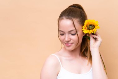 Bej arka planda izole edilmiş beyaz bir kız elinde bir ayçiçeği tutuyor. Portreyi kapat