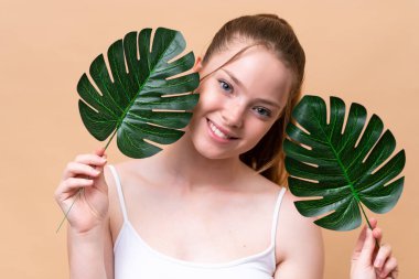 Beyaz tenli genç bir kız bej arka planda izole edilmiş elinde mutlu bir ifadeyle bir palmiye yaprağı tutuyor. Portreyi kapat