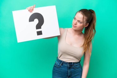Young caucasian woman isolated on green background holding a placard with question mark symbol