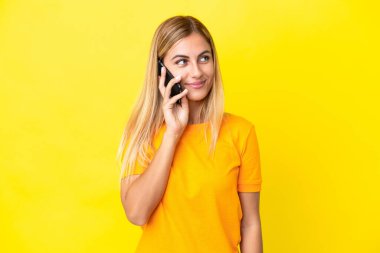 Sarışın Uruguaylı kız sarı arka planda izole edilmiş cep telefonuyla sohbet ediyor.