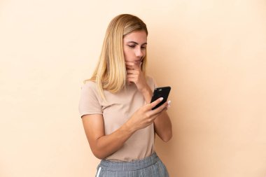 Blonde Uruguayan girl isolated on beige background thinking and sending a message