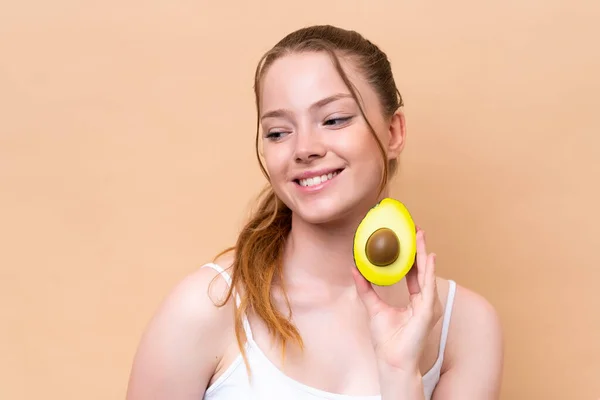 Young Caucasian Girl Isolated Beige Background Holding Avocado While Smiling — Stockfoto