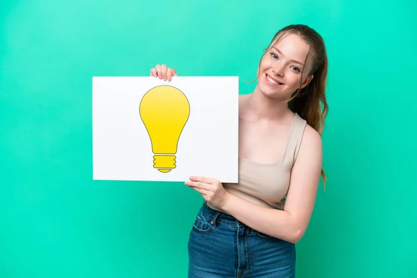 Young Caucasian Woman Isolated Green Background Holding Placard Bulb Icon — 图库照片