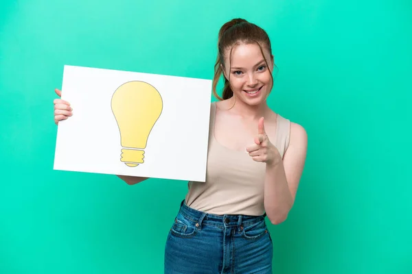 Young Caucasian Woman Isolated Green Background Holding Placard Bulb Icon — Zdjęcie stockowe