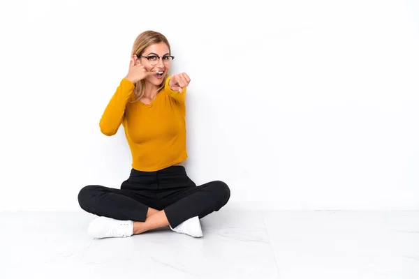 Blonde Uruguayan Girl Sitting Floor Making Phone Gesture Pointing Front — Stockfoto