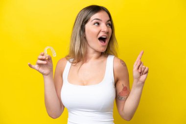 Young Rumanian woman holding envisaging isolated on yellow background intending to realizes the solution while lifting a finger up
