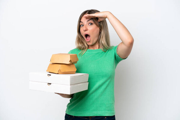 Young Rumanian woman holding fast-food isolated on white background doing surprise gesture while looking to the side