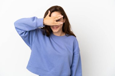 Beyaz arka planda soyutlanmış beyaz tenli genç bir kadın elleriyle gözlerini kapatıyor ve gülümsüyor.