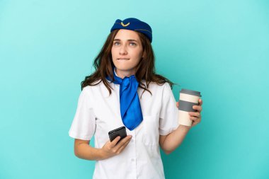 Uçak hostesi kadın mavi arka planda izole edilmiş. Elinde kahve ve bir şeyler düşünürken cep telefonu var.