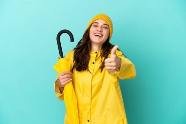 Mavi arka planda şemsiyesi olan beyaz bir adam var. Başparmakları havada. Çünkü iyi bir şey oldu.