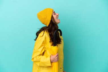 Mavi arka planda şemsiyesi olan genç beyaz adam yan pozisyonda gülüyor.