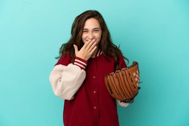 Beyzbol oynayan beyaz bir kadın mavi arka planda izole edilmiş mutlu ve ağzı kapalı gülümsüyor.