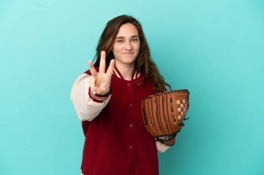 Beyzbol oynayan beyaz bir kadın mavi arka planda izole edilmiş mutlu ve parmaklarıyla üçe kadar sayıyor.