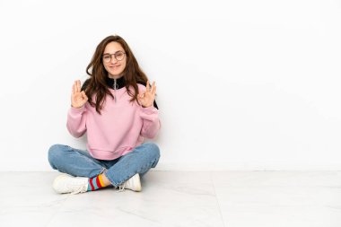 Beyaz arka planda izole bir şekilde yerde oturan genç beyaz kadın parmaklarıyla 