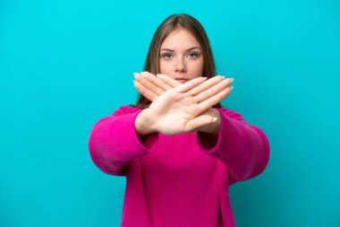 Genç Litvanyalı bir kadın mavi arka planda izole edilmiş bir şekilde bir eylemi durdurmak için el hareketi yapıyor.