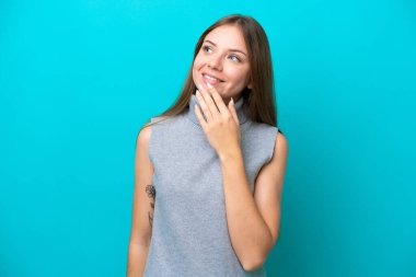 Genç Litvanyalı kadın mavi arka planda izole edilmiş gülümserken yukarı bakıyor