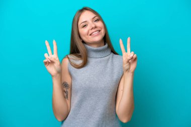 Mavi arka planda izole edilmiş genç Litvanyalı kadın iki eliyle zafer işareti gösteriyor.