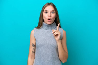 Genç Litvanyalı bir kadın mavi arka planda izole edilmiş bir şekilde parmağını kaldırarak çözümü anlamaya çalışıyor.