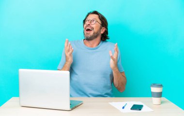 Masada dizüstü bilgisayarı olan yaşlı bir Hollandalı, mavi arka planda, sürpriz bir yüz ifadesiyle izole edilmiş.