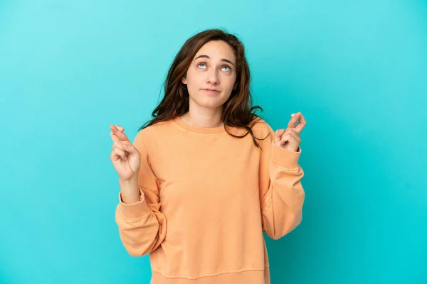 Young caucasian woman isolated on blue background with fingers crossing and wishing the best