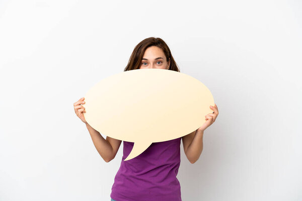 Молодая белая женщина, изолированная на белом фоне, держит пустой пузырь речи, прячащийся за ним.