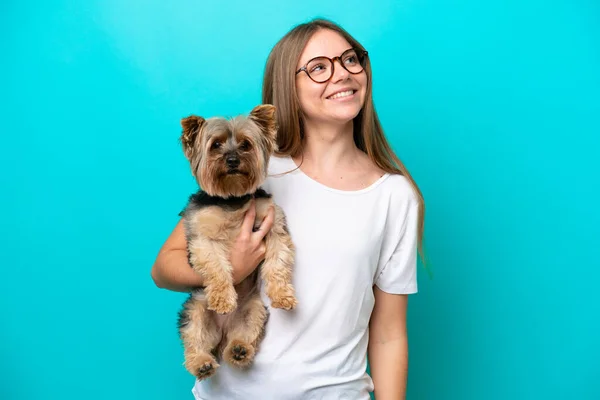Young Lithuanian woman holding a dog isolated on blue background looking up while smiling