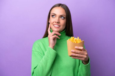 Young caucasian woman holding fried chips on purple background thinking an idea while looking up
