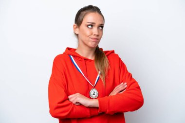 Beyaz arka planda madalyaları olan genç beyaz bir kadın omuzlarını kaldırırken şüpheyle hareket ediyor.