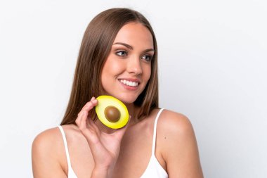 Beyaz arka planda izole edilmiş beyaz bir kadın elinde bir avokado tutarken gülümsüyor. Portreyi kapat