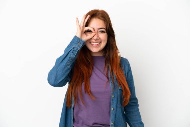 Beyaz arka planda izole edilmiş genç kızıl saçlı kadın parmaklarıyla işaret veriyor.