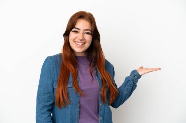 Beyaz arka planda izole edilmiş genç, kızıl saçlı bir kadın. Bir ilan vermek için avucunda hayali bir şey tutuyor.