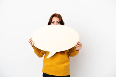 Young redhead woman isolated on white background holding an empty speech bubble hiding behind it hiding behind it