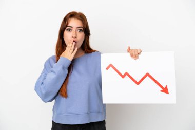 Young redhead woman isolated on white background holding a sign with a decreasing statistics arrow symbol with surprised expression