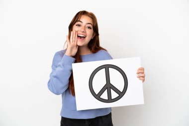 Young redhead woman isolated on white background holding a placard with peace symbol and shouting