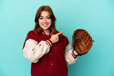 Beyzbol oynayan genç kızıl saçlı kadın, mavi arka planda soyutlanmış bir şekilde bir ürünü sunmak için kenarı işaret ediyor.