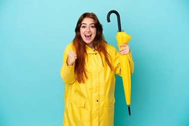 Mavi arka planda şemsiyesi olan kızıl saçlı kadın zaferi kutluyor.