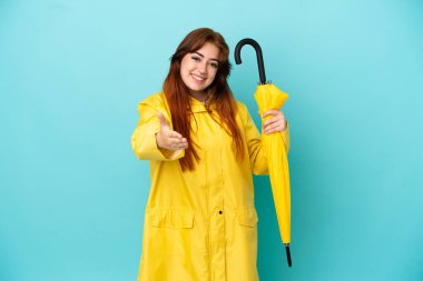 Mavi arka planda şemsiyesi olan kızıl saçlı kadın iyi bir anlaşma için el sıkışıyor.
