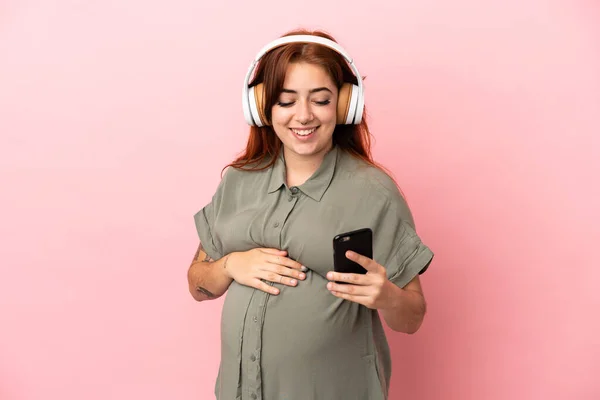 Young Redhead Caucasian Woman Isolated Pink Background Pregnant Listening Music — Stock Fotó