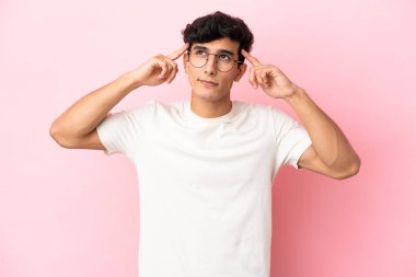 Arjantinli genç bir adam pembe arka planda izole edilmiş. Şüpheleri ve düşünceleri var.