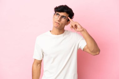 Arjantinli genç bir adam pembe arka planda izole edilmiş. Delilik hareketi yapıyor. Parmağını kafaya koyuyor.