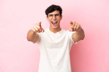 Pembe arka planda izole edilmiş genç Arjantinli adam şaşırmış ve ön tarafı işaret ediyor.