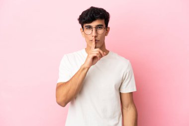 Pembe arka planda izole edilmiş genç Arjantinli bir adam sessizlik işareti gösteriyor. Parmağını ağzına sokuyor.