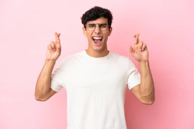 Arjantinli genç adam pembe arka planda izole edilmiş ve parmakları çapraz