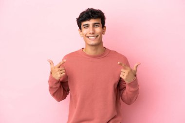 Pembe arka planda izole edilmiş genç Arjantinli bir adam baş parmak hareketi yapıyor.