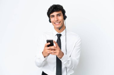 Beyaz arka planda izole edilmiş bir kulaklıkla çalışan pazarlamacı cep telefonuyla bir mesaj gönderiyor.