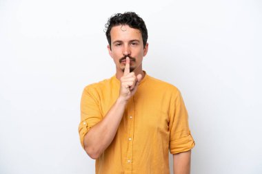 Bıyıklı genç adam beyaz arka planda izole edilmiş. Sessiz bir jest işareti gösteriyor. Parmağını ağzına sokuyor.